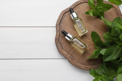 Photo of Bottles of essential oil and mint on white wooden table, top view. Space for text