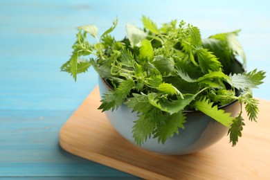 Photo of Fresh stinging nettle leaves in bowl on light blue wooden table, closeup