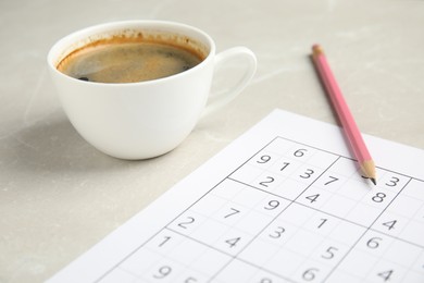 Photo of Sudoku, cup of coffee and pencil on light marble table, closeup