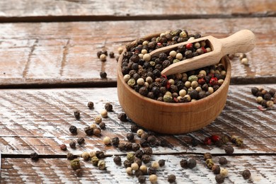 Photo of Aromatic spice. Different peppers in bowl and scoop on wooden table, space for text