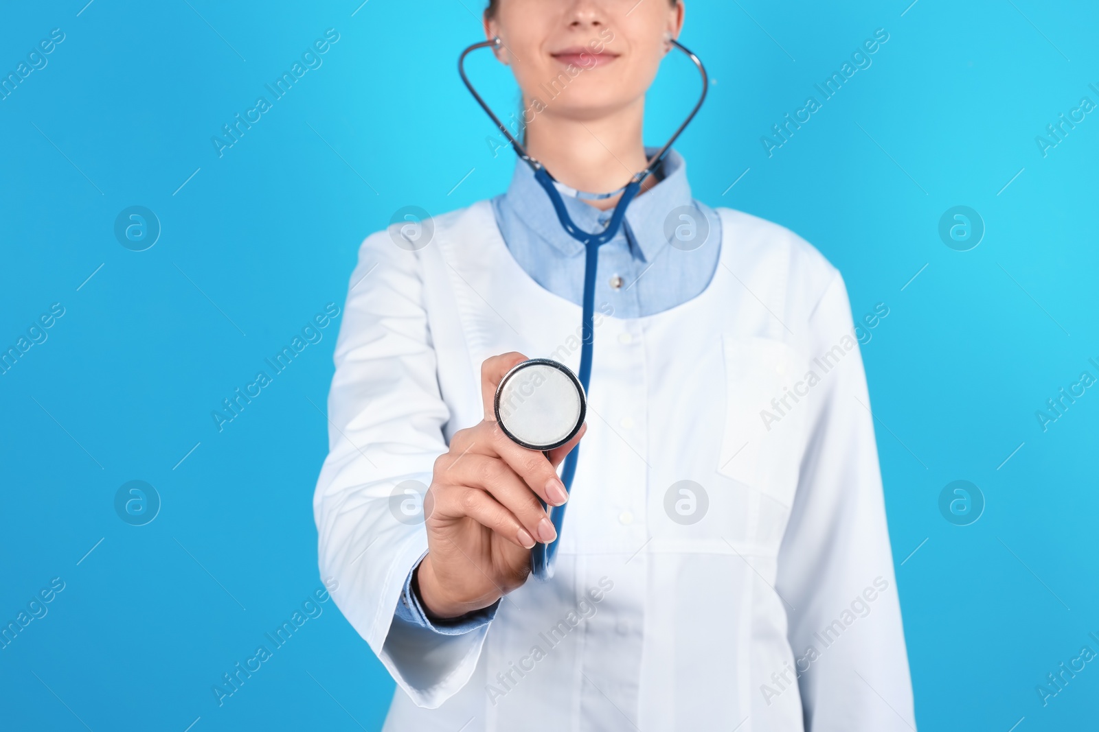 Photo of Female doctor holding stethoscope on color background, closeup