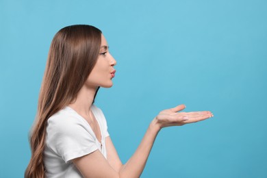 Beautiful young woman blowing kiss on light blue background, space for text