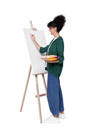 Young woman painting on easel with canvas against white background