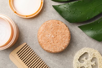 Photo of Solid shampoo bar, cream, monstera leaf, comb and loofah on grey table, flat lay