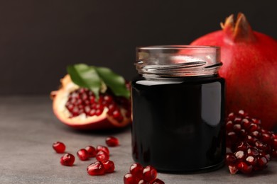 Photo of Glass jar of tasty pomegranate sauce and fresh ripe fruit on light grey table. Space for text