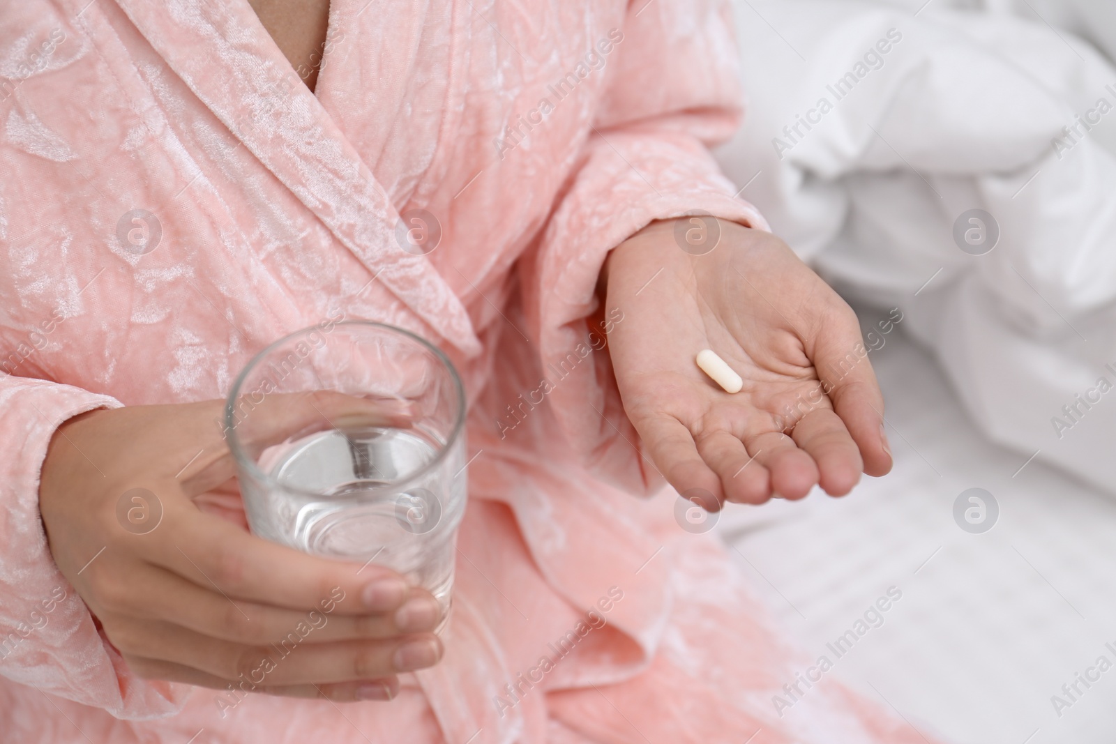 Photo of Woman holding glass of water and pill in bedroom, closeup