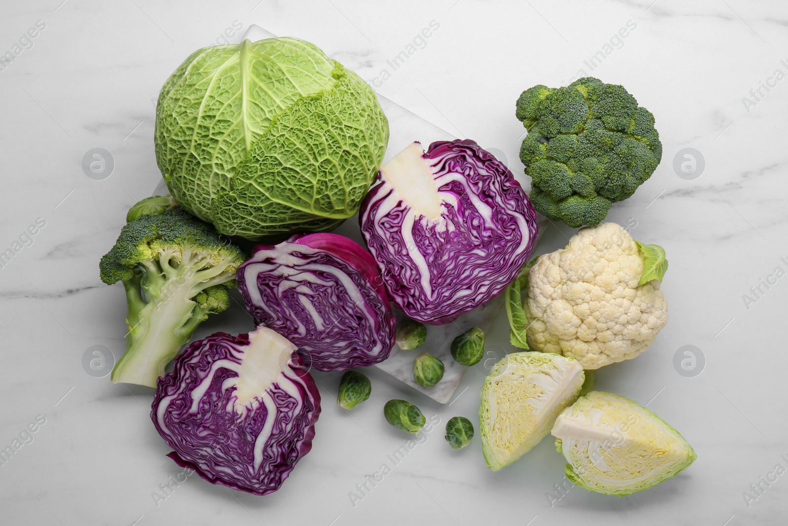 Photo of Many different cabbage types on white marble table, flat lay