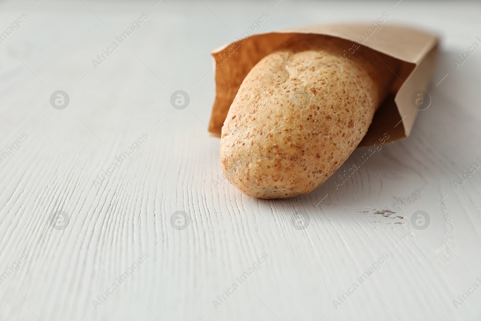 Photo of Baguette in paper bag on wooden table, closeup. Space for text