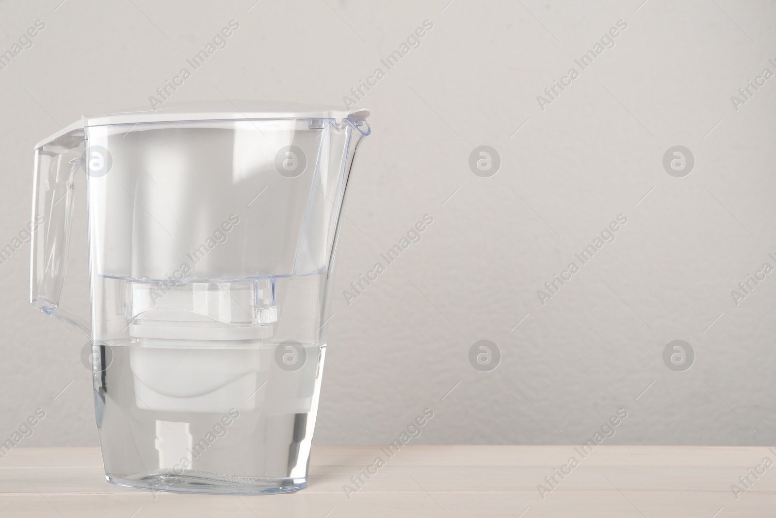 Photo of Filter jug with purified water on white table against light background. Space for text