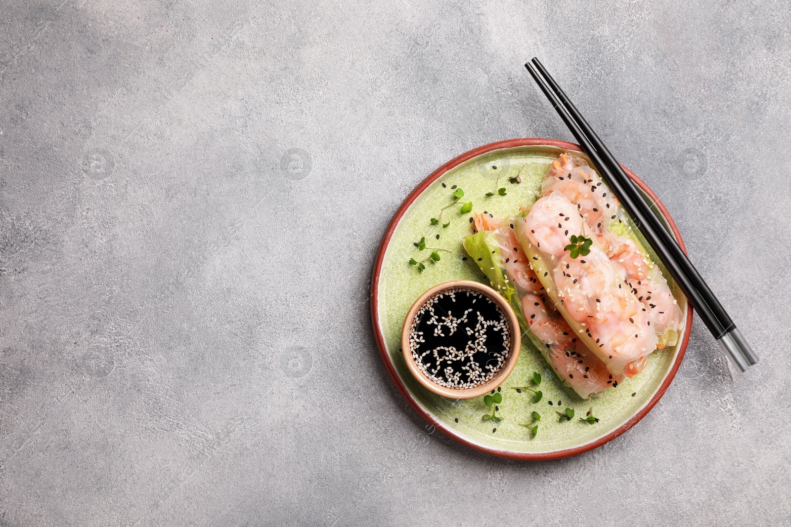 Photo of Plate with tasty spring rolls served with soy sauce on grey textured table, top view. Space for text