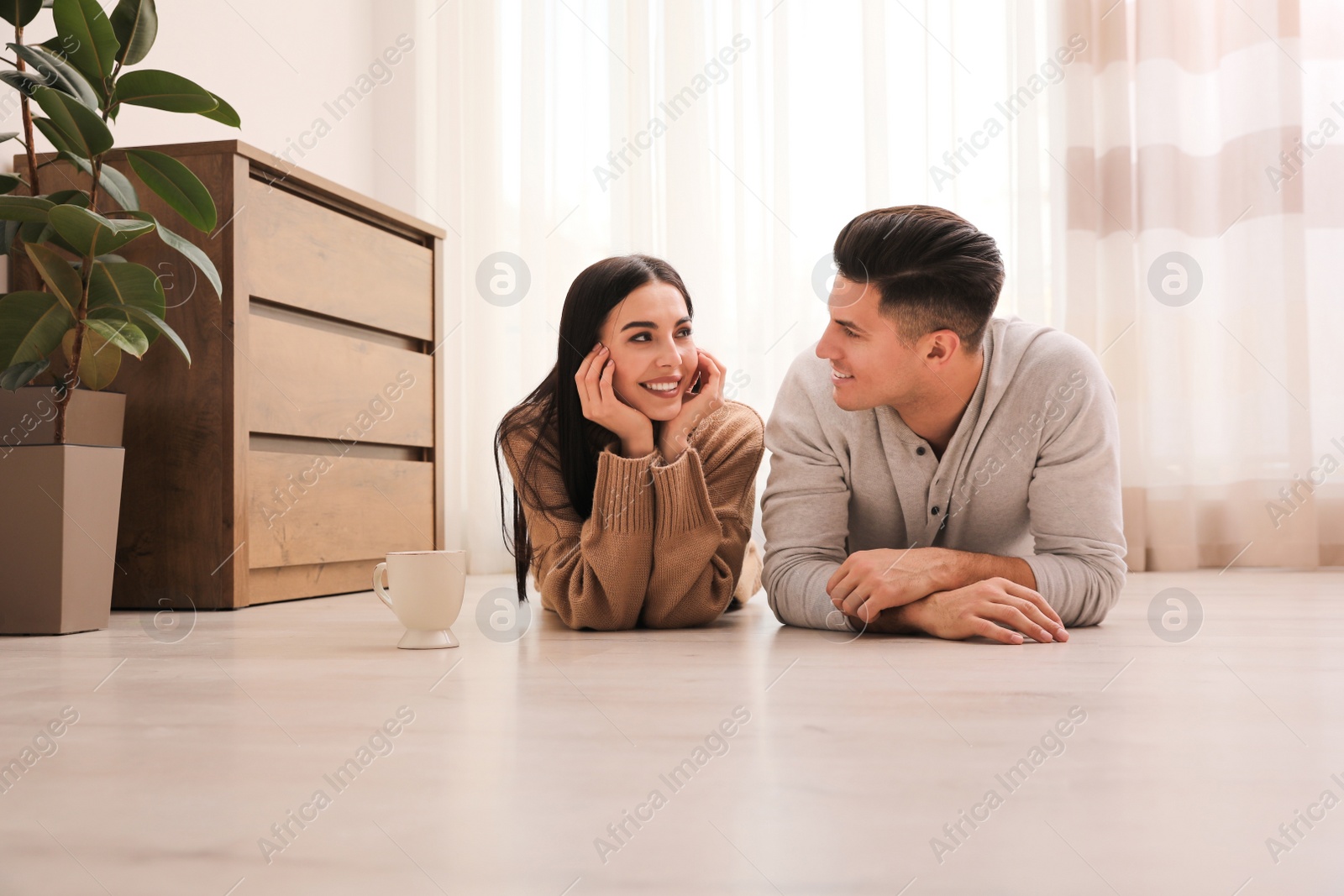 Photo of Happy couple lying on warm floor at home. Heating system