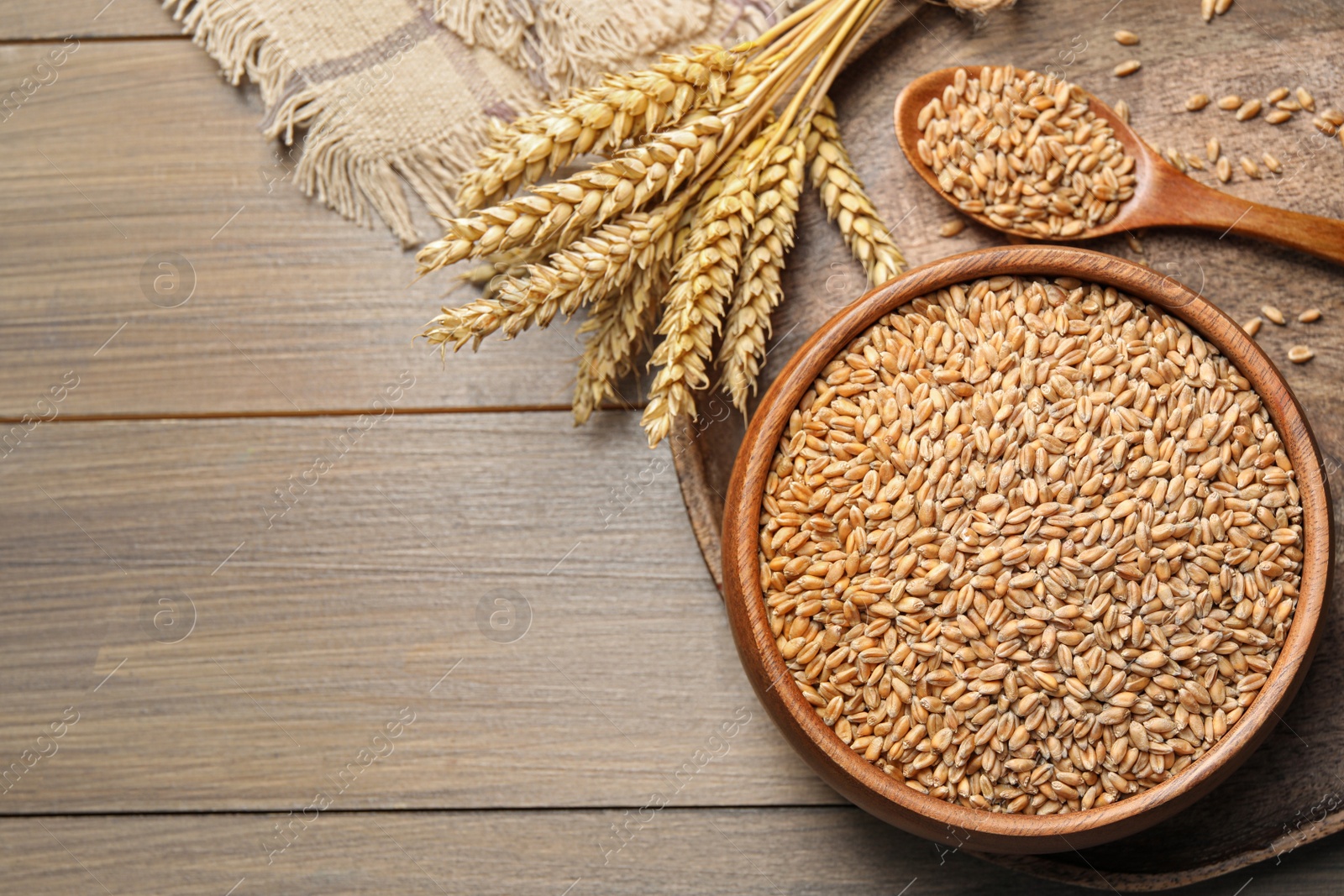 Photo of Wheat grains in bowl, spoon and spikes on wooden table, flat lay. Space for text