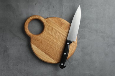 Photo of Knife and wooden board on grey textured table, top view