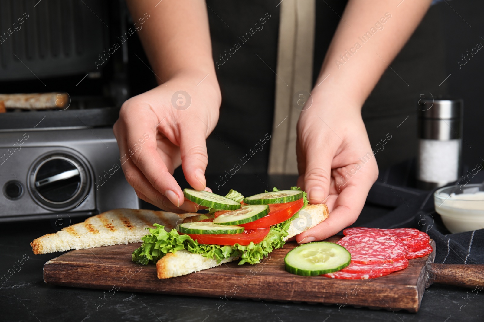 Photo of Woman adding cucumber to sandwich at black table, closeup