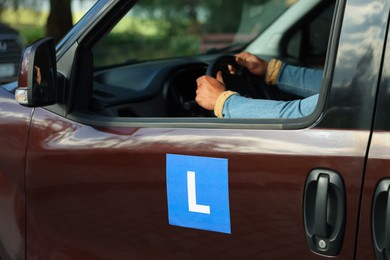 Learner driver driving car with L-plate, view from outside. Driving school