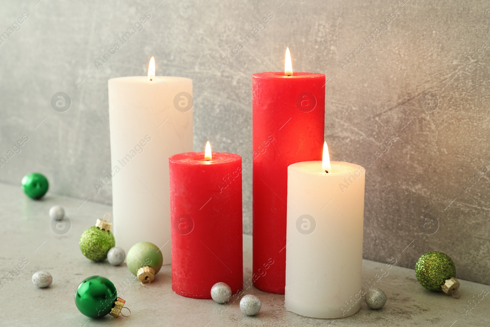 Photo of Burning candles with Christmas baubles on light grey table