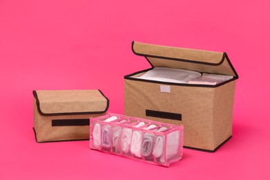 Photo of Textile storage cases and organizer with folded clothes on pink background