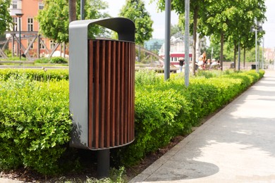 Trash bin near green bushes in park on sunny day, space for text