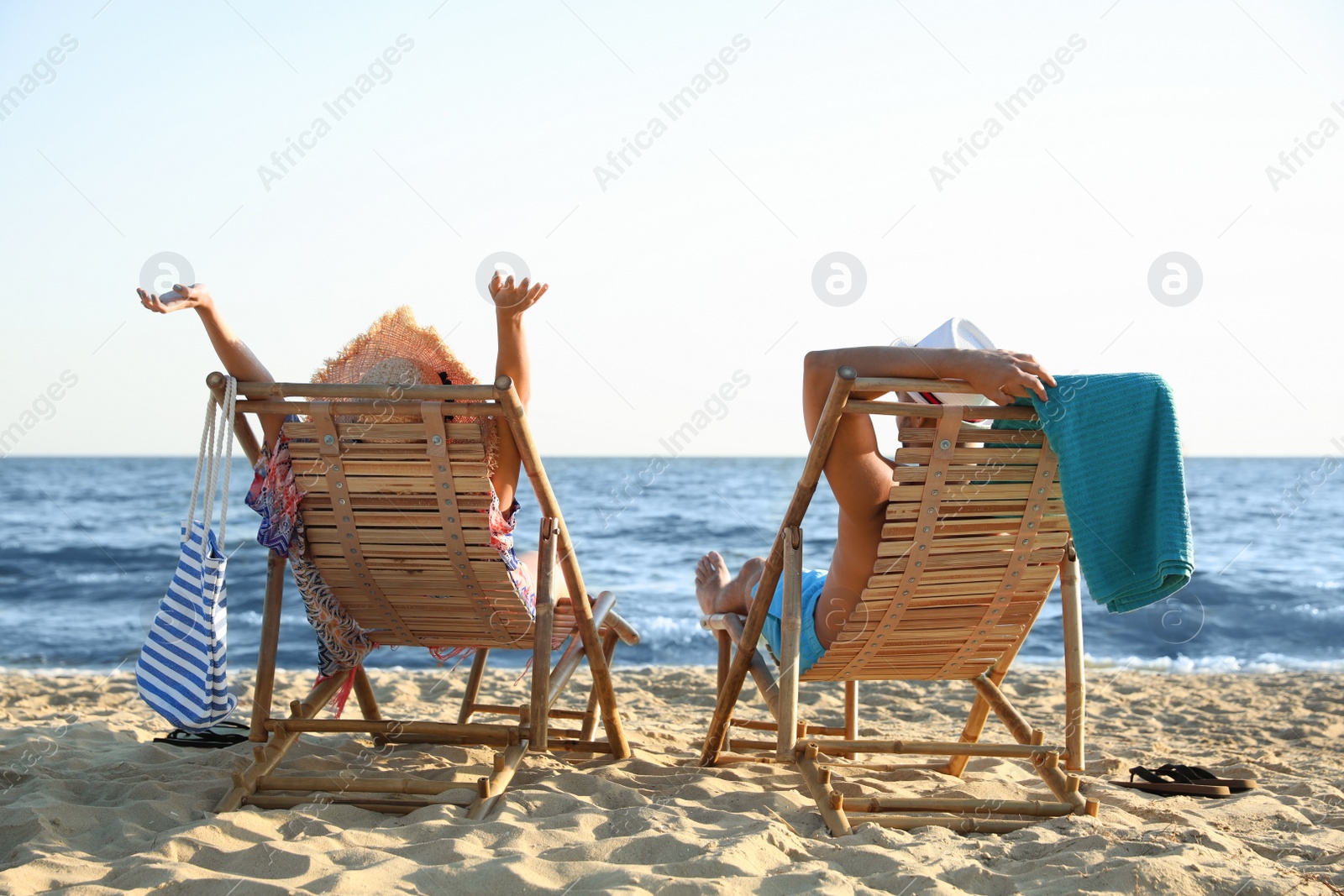 Photo of Young couple relaxing in deck chairs on beach near sea