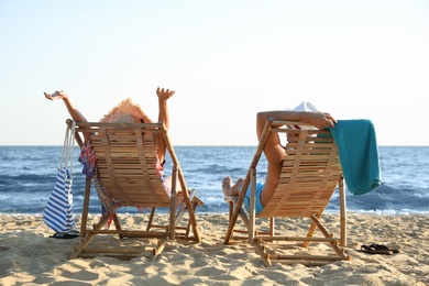 Young couple relaxing in deck chairs on beach near sea