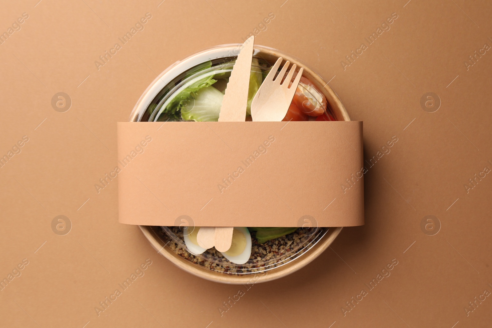 Photo of Tasty food in container with wooden fork and knife on beige background, top view. Space for text