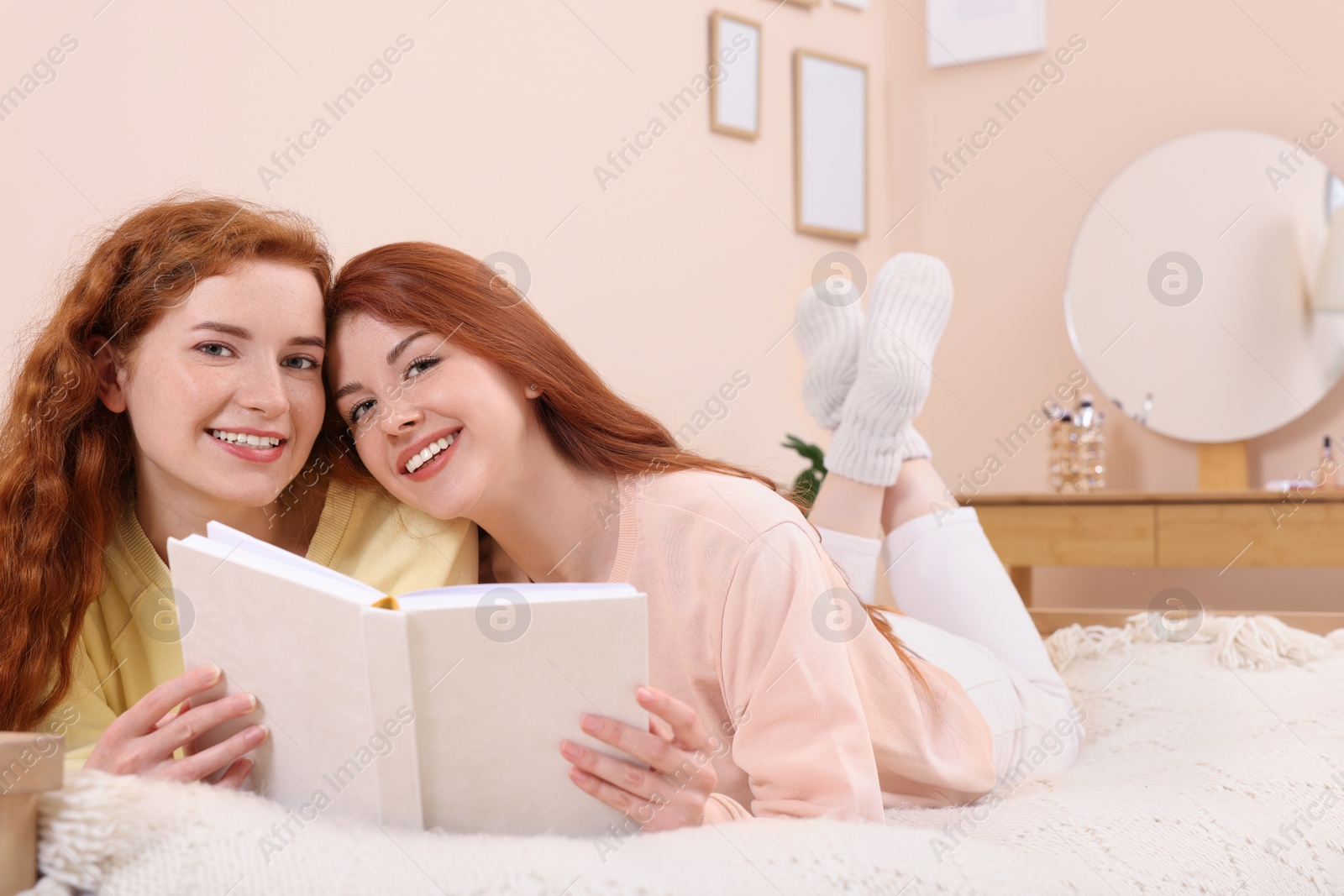 Photo of Portrait of beautiful young sisters with book on bed at home