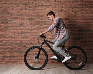 Photo of Handsome young man with modern bicycle near brick wall indoors