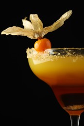 Tasty cocktail decorated with physalis fruit on black background, closeup