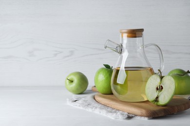Photo of Jug of tasty juice and fresh ripe green apples on white wooden table, space for text