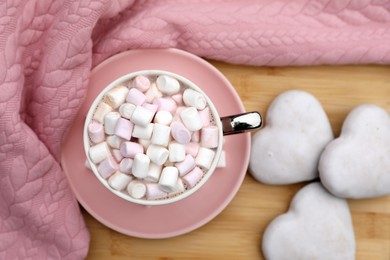 Cup of tasty cocoa with marshmallows, pink sweater and cookies on wooden table, flat lay