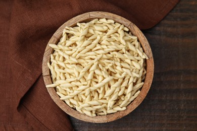 Uncooked trofie pasta in bowl on wooden table, top view
