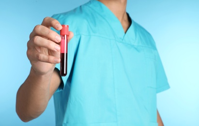Photo of Male doctor holding test tube with blood sample on color background, closeup. Medical object