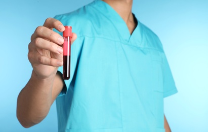 Male doctor holding test tube with blood sample on color background, closeup. Medical object