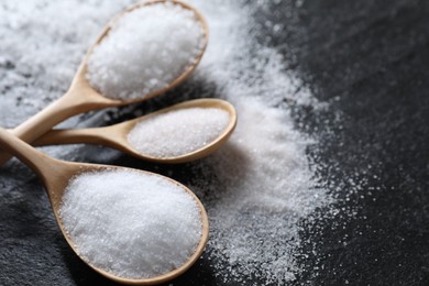 Photo of Organic salt in spoons on black table, closeup. Space for text