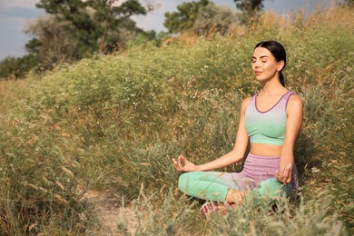 Photo of Young woman meditating on hill. Space for text