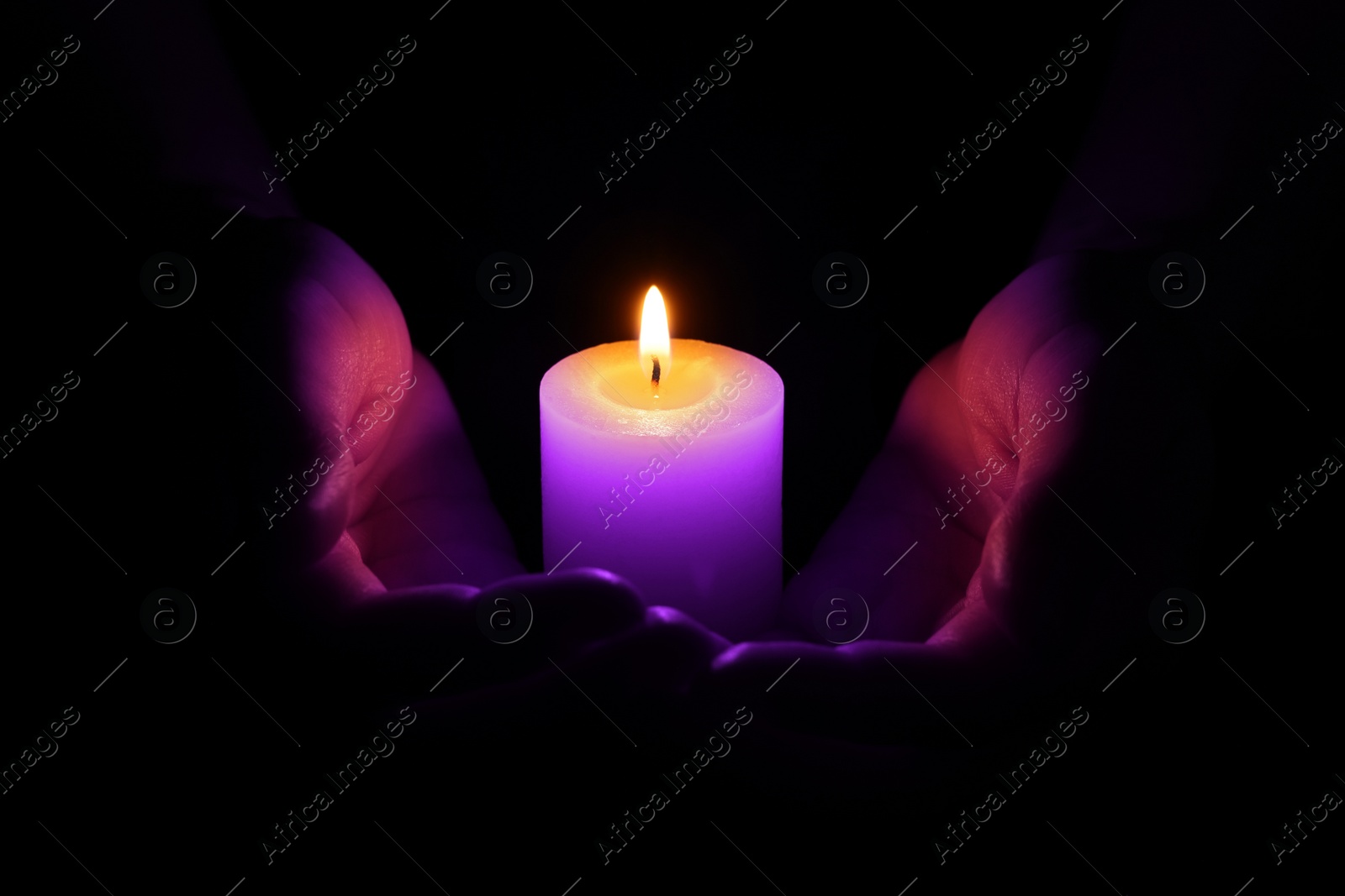 Image of Woman holding burning violet candle in hands on black background, closeup. Funeral attributes