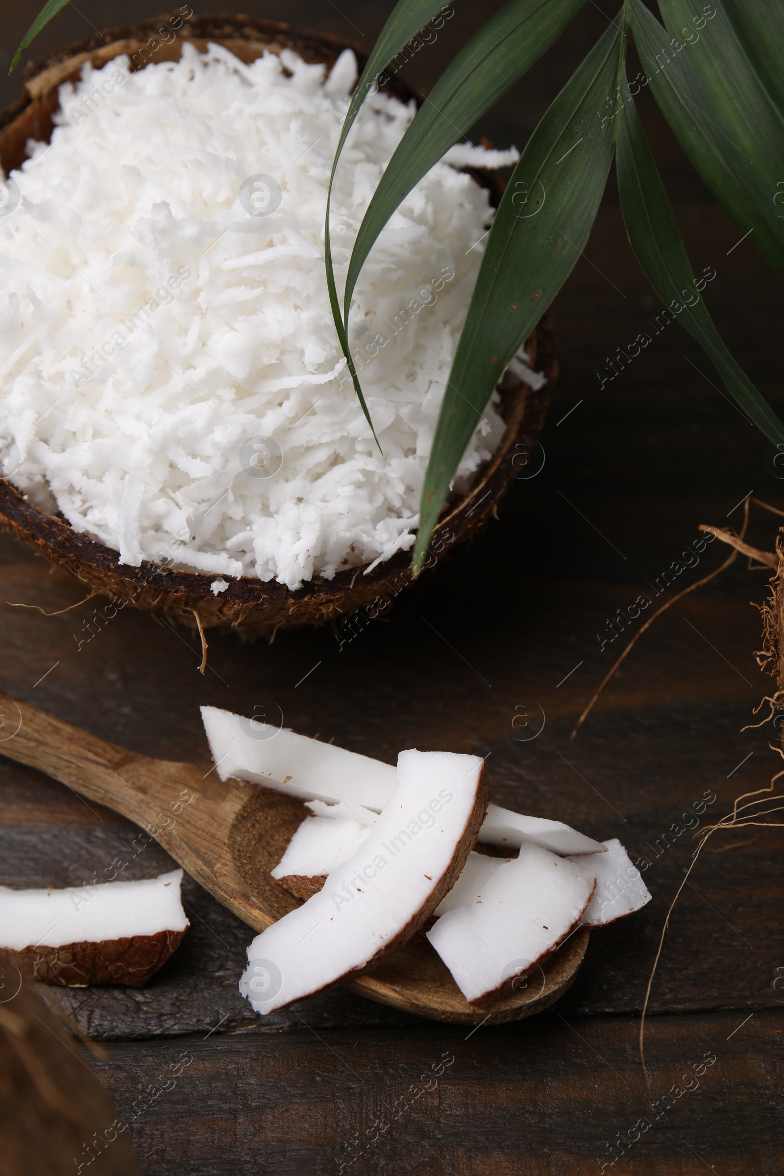 Photo of Coconut flakes, spoon, nut and palm leaf on wooden table