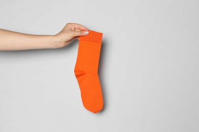 Photo of Woman holding orange sock against grey background, closeup