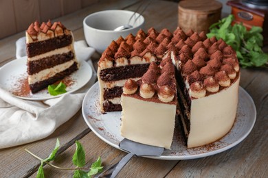 Delicious tiramisu cake with mint leaves and server on wooden table