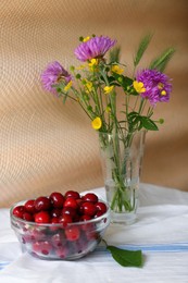 Photo of Bouquet of beautiful wildflowers and sweet cherries on table