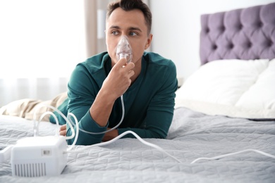 Young man with asthma machine on bed in light room