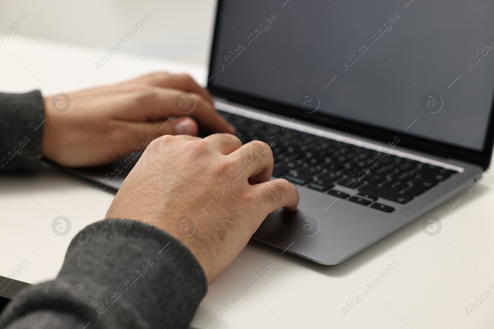 Photo of E-learning. Young man using laptop at white table, closeup