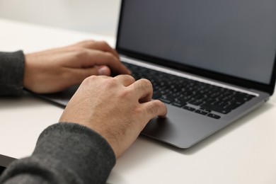 Photo of E-learning. Young man using laptop at white table, closeup