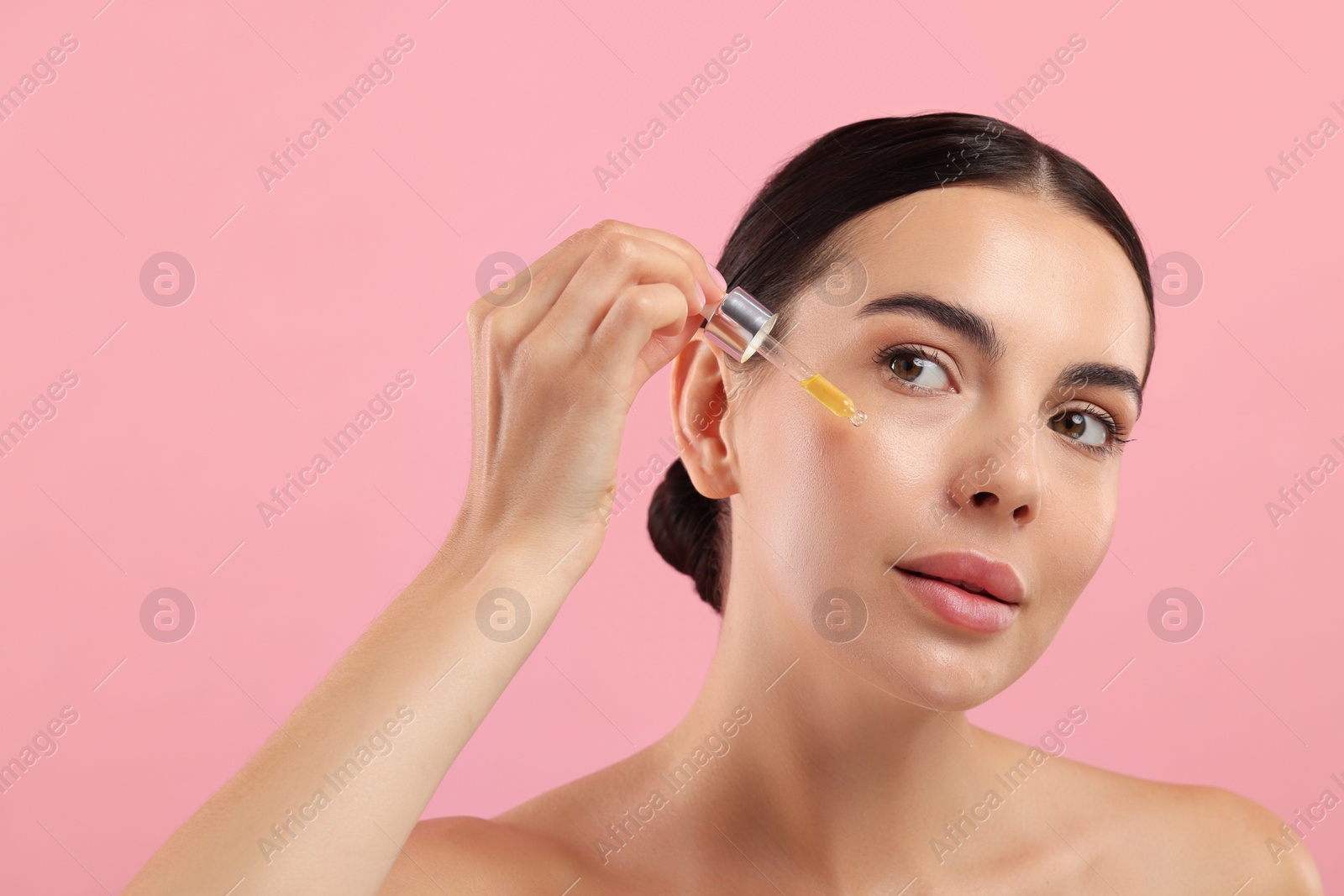 Photo of Beautiful young woman applying serum onto her face on pink background