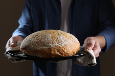 Photo of Man holding loaf of fresh bread on dark background, closeup