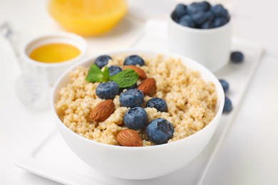 Photo of Bowl of delicious cooked quinoa with almonds and blueberries on white table, closeup