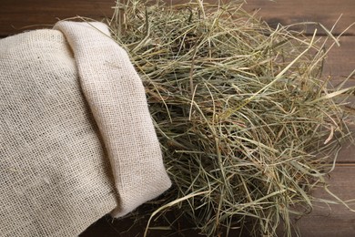 Photo of Dried hay in burlap sack on wooden table, closeup
