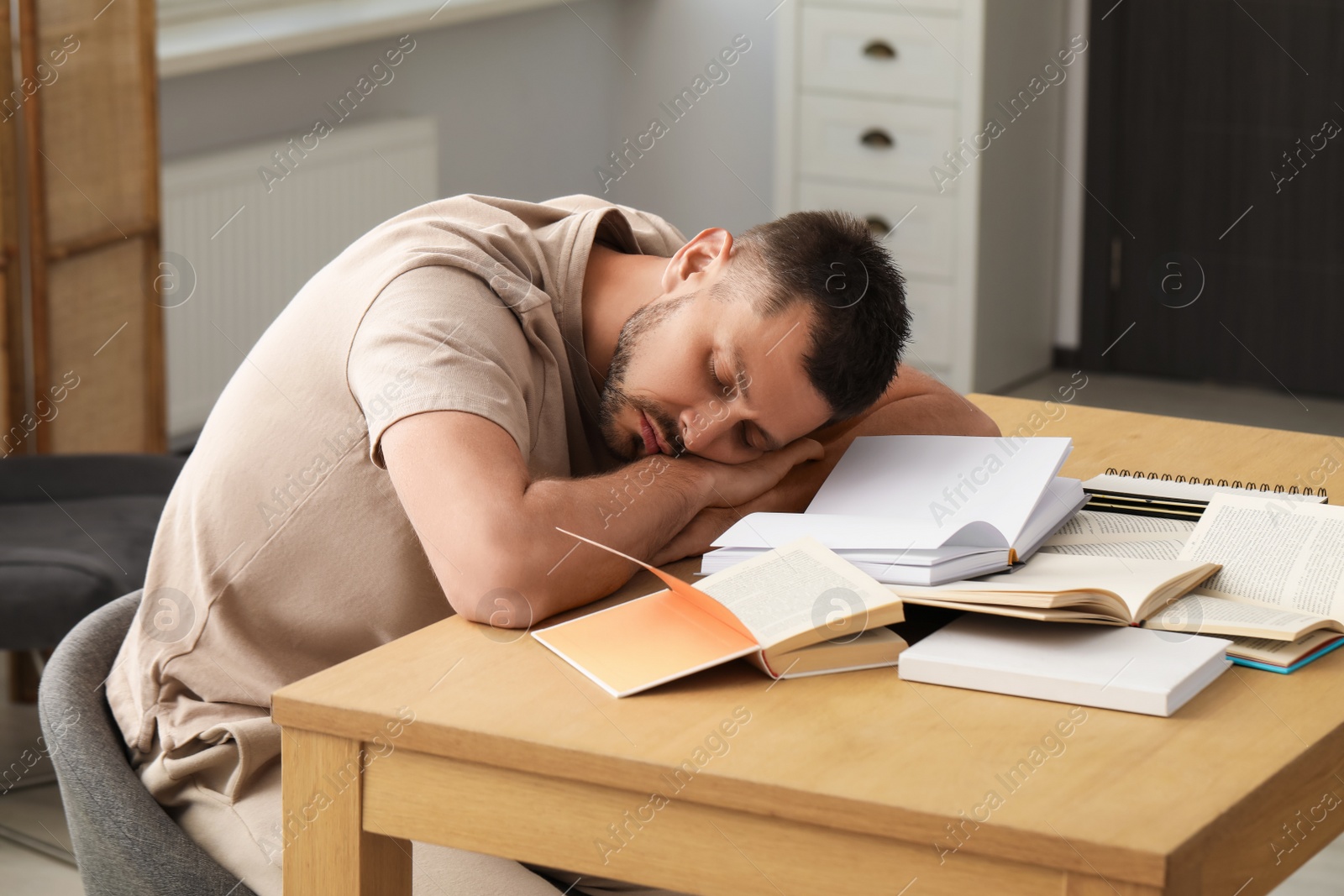 Photo of Tired man sleeping among books at wooden table indoors