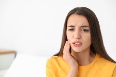 Young woman suffering from strong tooth pain at home, space for text