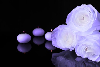 Violet roses and burning candles on black mirror surface, space for text. Funeral attributes